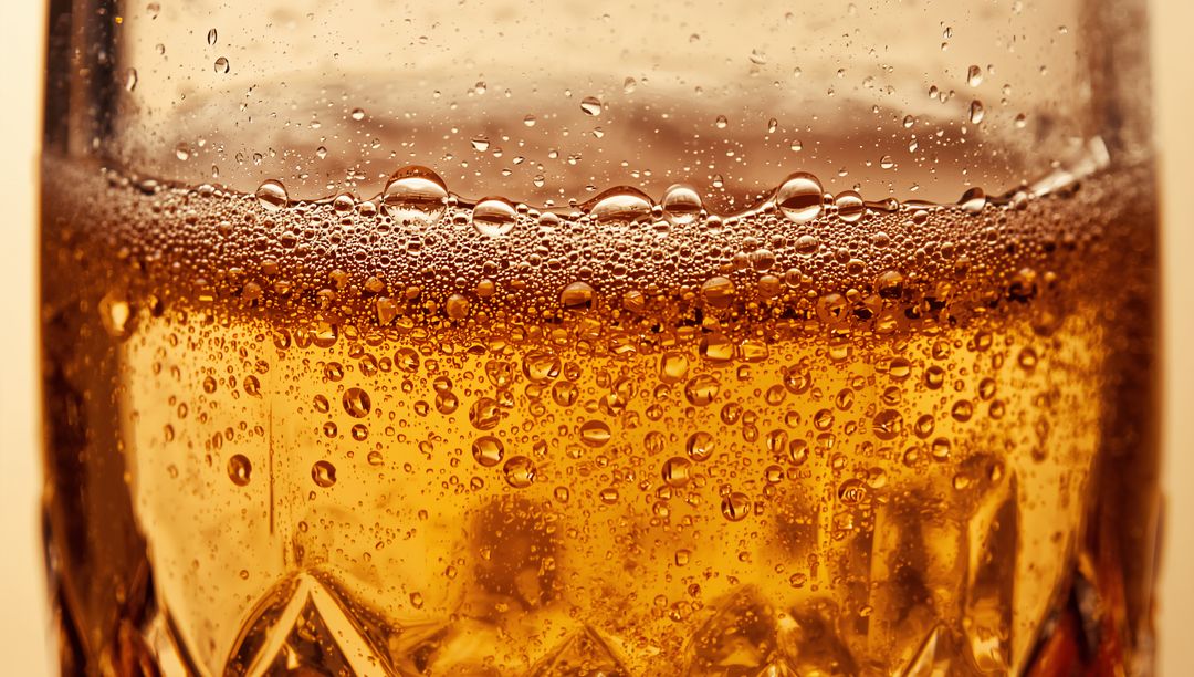 Macro Amber Drink Bubbling in Cut-Glass Tumbler with Foamy Head and Effervescence