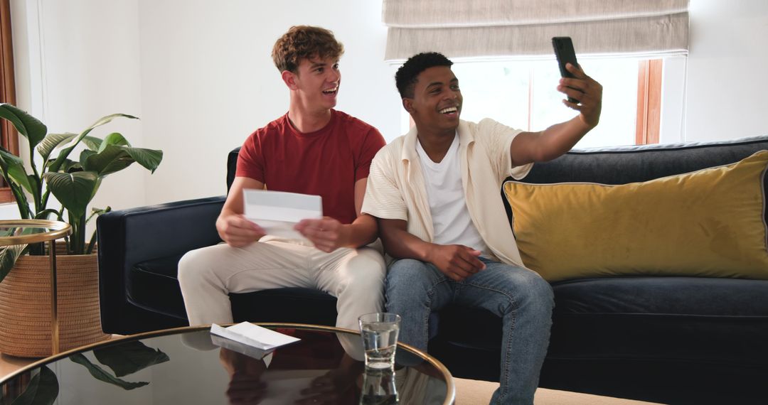 Diverse friends taking selfie on modern navy sofa while opening greeting card and laughing