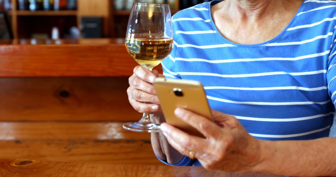 Senior Woman Holding Wine Glass Using Smartphone in Rustic Cafe - Free Images, Stock Photos and Pictures on Pikwizard.com