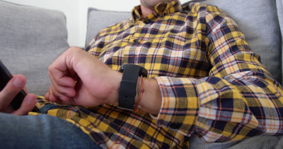 Man using smartphone while checking smartwatch on couch - Free Images, Stock Photos and Pictures on Pikwizard.com