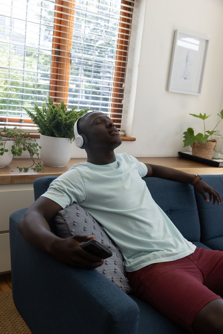 Young Man Relaxing on Sofa Listening to Music at Home