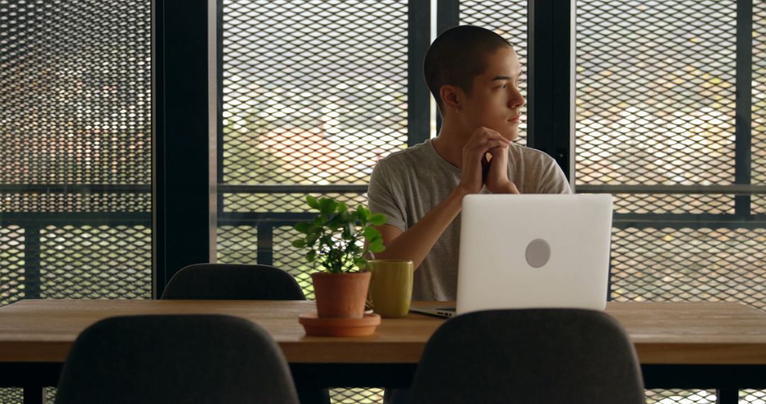 Young Man Wistfully Looking Out Window at Desk with Laptop - Free Images, Stock Photos and Pictures on Pikwizard.com