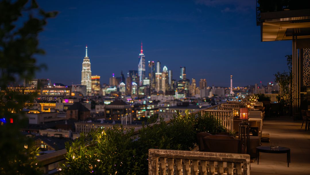 Rooftop terrace overlooking illuminated skyline at dusk with lantern-lit seating