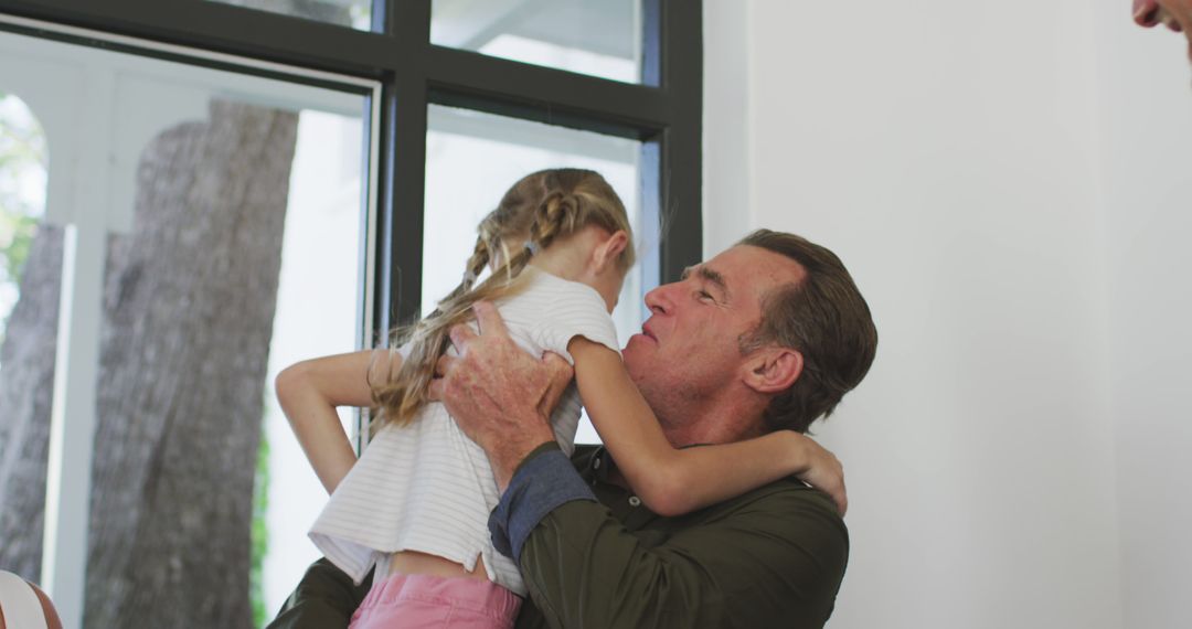 Grandfather Hugging Granddaughter Near Window at Home - Free Images, Stock Photos and Pictures on Pikwizard.com