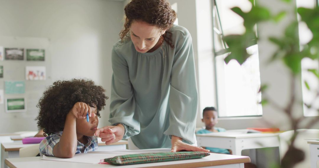 Teacher Leaning Over Student Assisting with Writing in Sunlit Modern Classroom