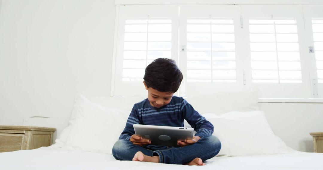 Child Enjoying Digital Tablet in Bright Bedroom - Free Images, Stock Photos and Pictures on Pikwizard.com