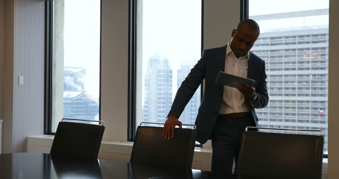 Businessman Reviewing Documents on Tablet Near Large Windows - Free Images, Stock Photos and Pictures on Pikwizard.com