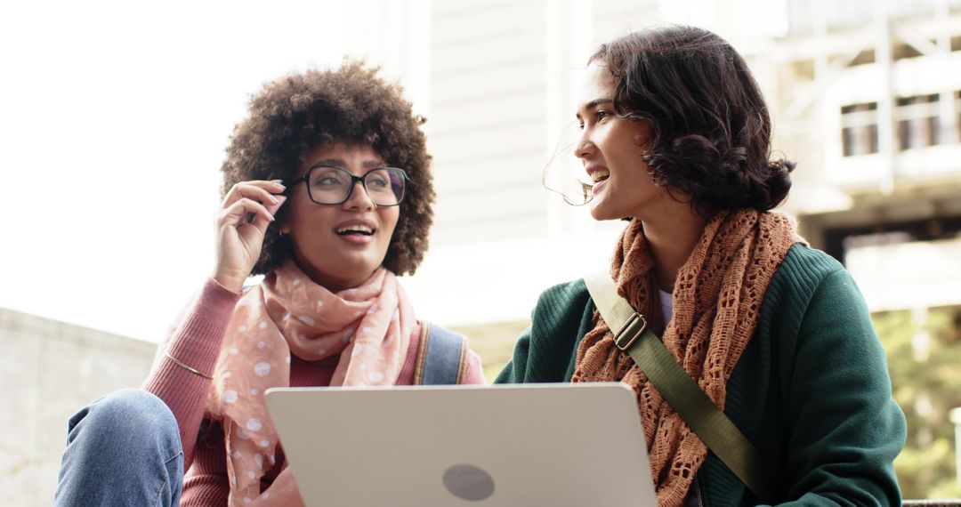 Multicultural students collaborating on laptop while laughing on campus steps