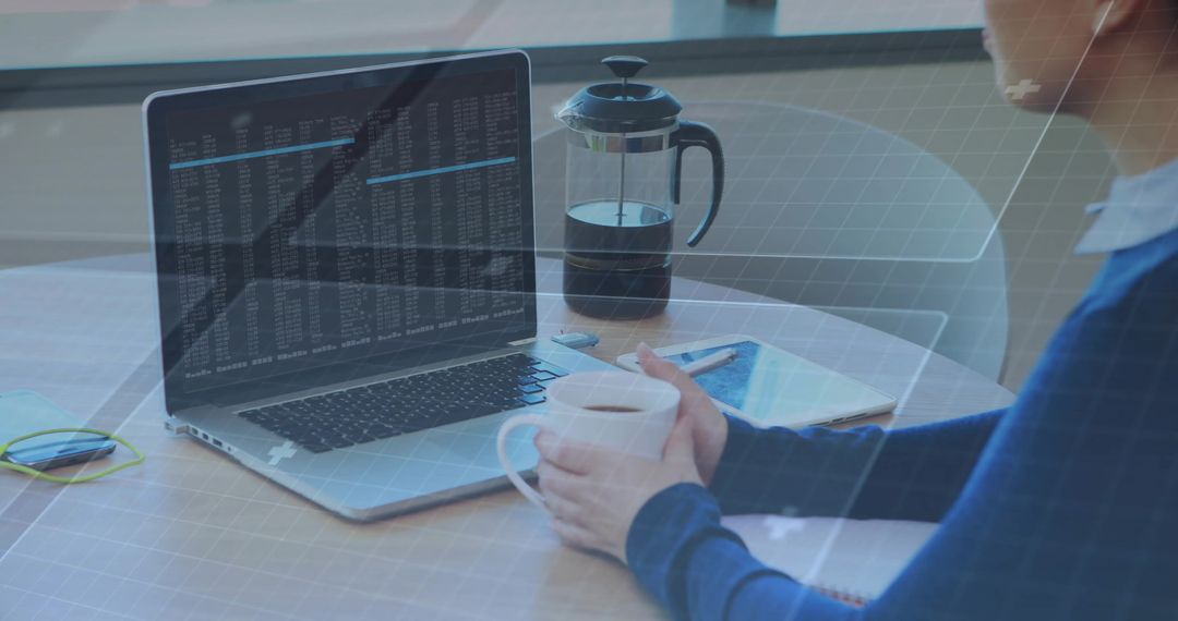Working from home woman holding coffee mug while coding on laptop with tablet nearby in daylight