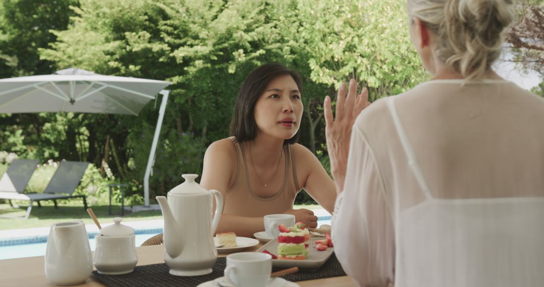 Two Friends Having Outdoor Conversation at Poolside Table