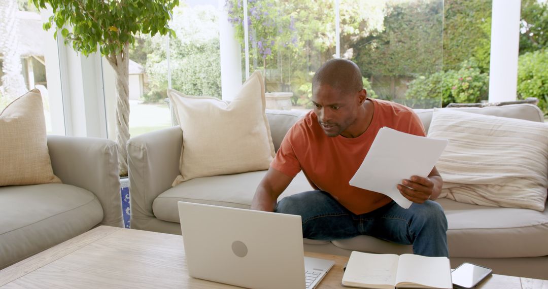 Man Analyzing Documents Working on Laptop at Home