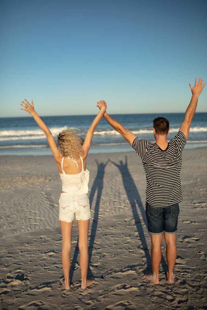 Couple Celebrating on Beach with Arms Raised - Free Images, Stock Photos and Pictures on Pikwizard.com