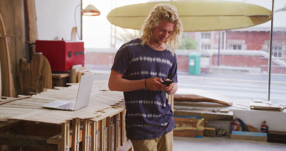 Smiling Young Man in Workshop Texting on Smartphone - Free Images, Stock Photos and Pictures on Pikwizard.com