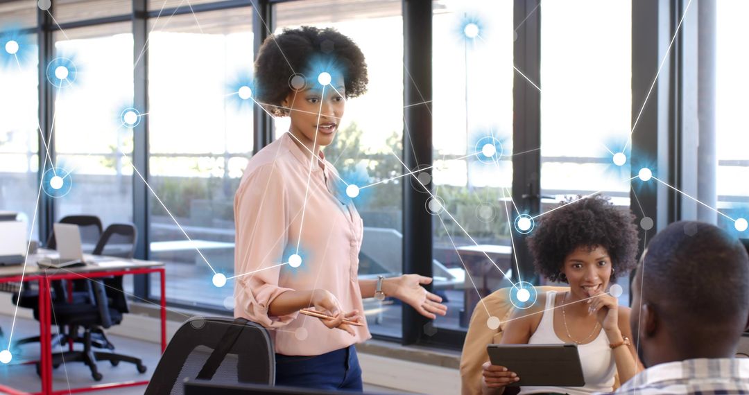 Leading collaborative meeting in open-plan office, gesturing woman with tablet and network graphic