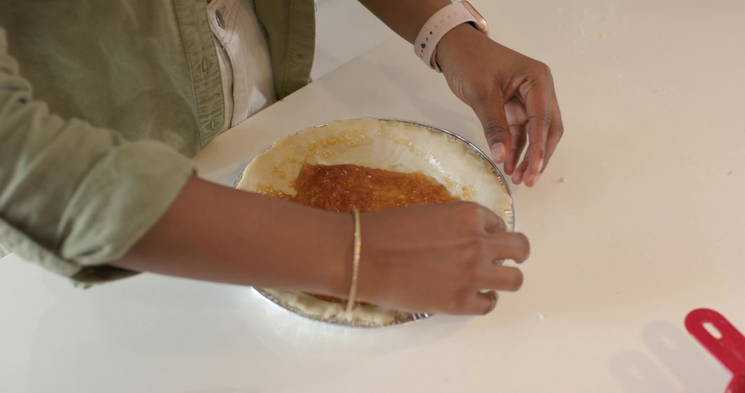 African American woman pressing pie crust with jam filling into tin on kitchen counter