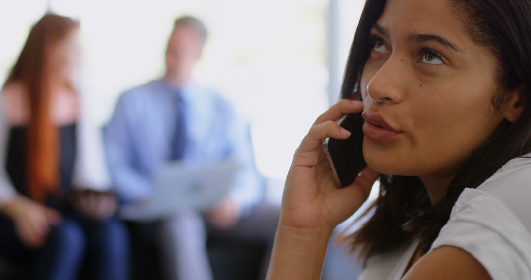 Businesswoman Discussing on Phone with Colleagues in Background - Free Images, Stock Photos and Pictures on Pikwizard.com