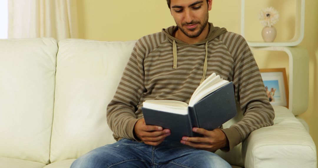 Young Man Reading a Book on a Sofa at Home - Free Images, Stock Photos and Pictures on Pikwizard.com