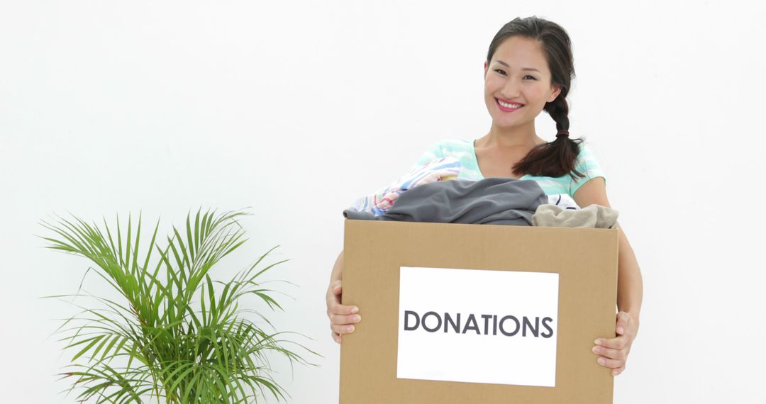 Smiling Woman Holding Donation Box with Clothes Contribution Theme - Free Images, Stock Photos and Pictures on Pikwizard.com