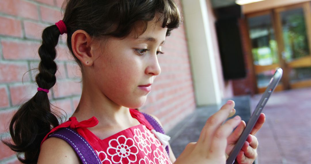 Young Girl with Pigtails Focused on Digital Tablet Outdoors - Free Images, Stock Photos and Pictures on Pikwizard.com