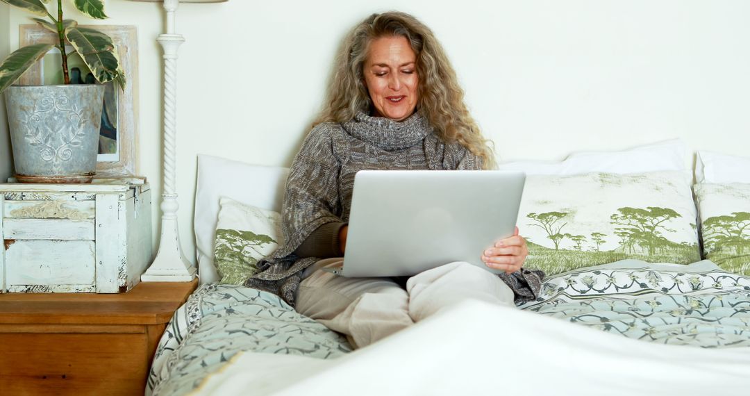 Smiling Mature Woman Using Laptop in Cozy Bedroom - Free Images, Stock Photos and Pictures on Pikwizard.com