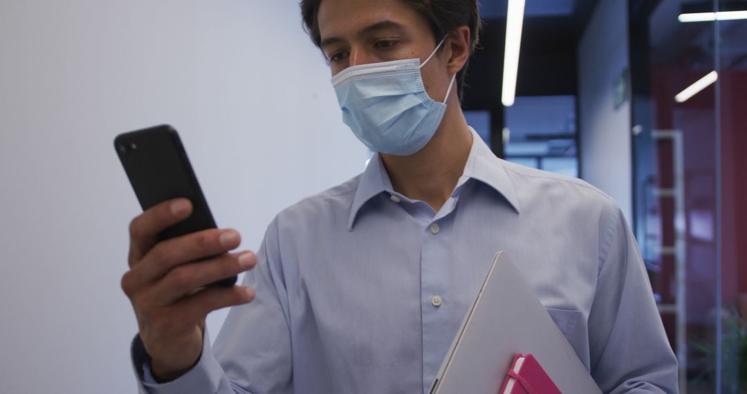 Businessman Wearing Mask Using Smartphone in Office Hallway - Free Images, Stock Photos and Pictures on Pikwizard.com