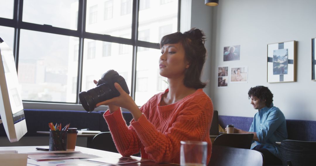 Biracial businesswoman sitting at table and inspecting camera at office - Free Images, Stock Photos and Pictures on Pikwizard.com