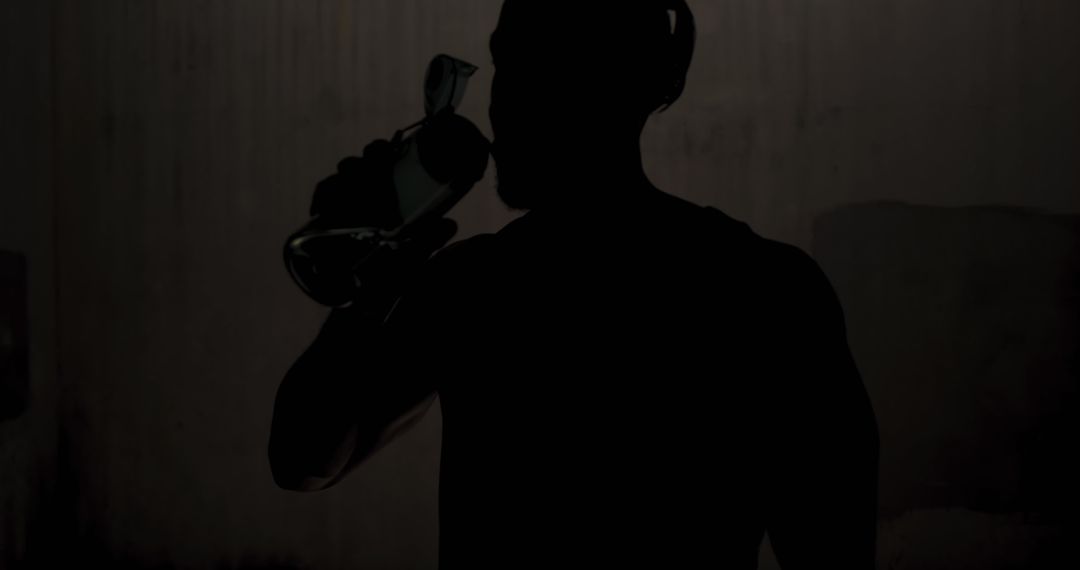 Silhouette of Man Drinking from a Bottle in Dark Setting - Free Images, Stock Photos and Pictures on Pikwizard.com