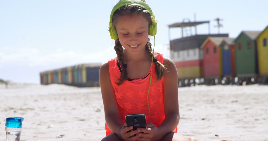 Young Girl Enjoying Music on Beachside with Colorful Huts in Background - Free Images, Stock Photos and Pictures on Pikwizard.com