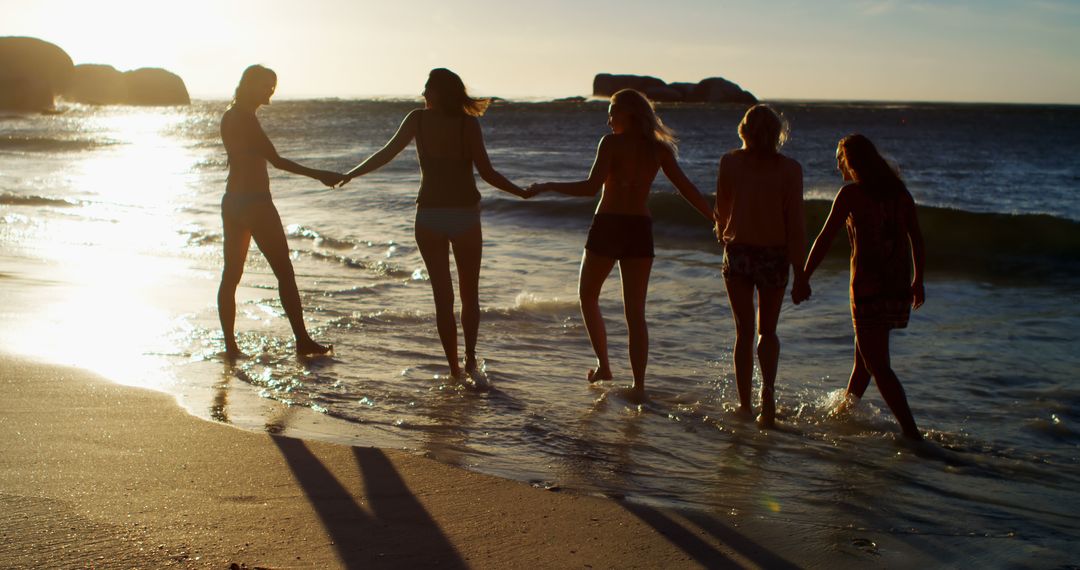 Group of Friends Holding Hands Walking Along Beach at Sunset - Free Images, Stock Photos and Pictures on Pikwizard.com