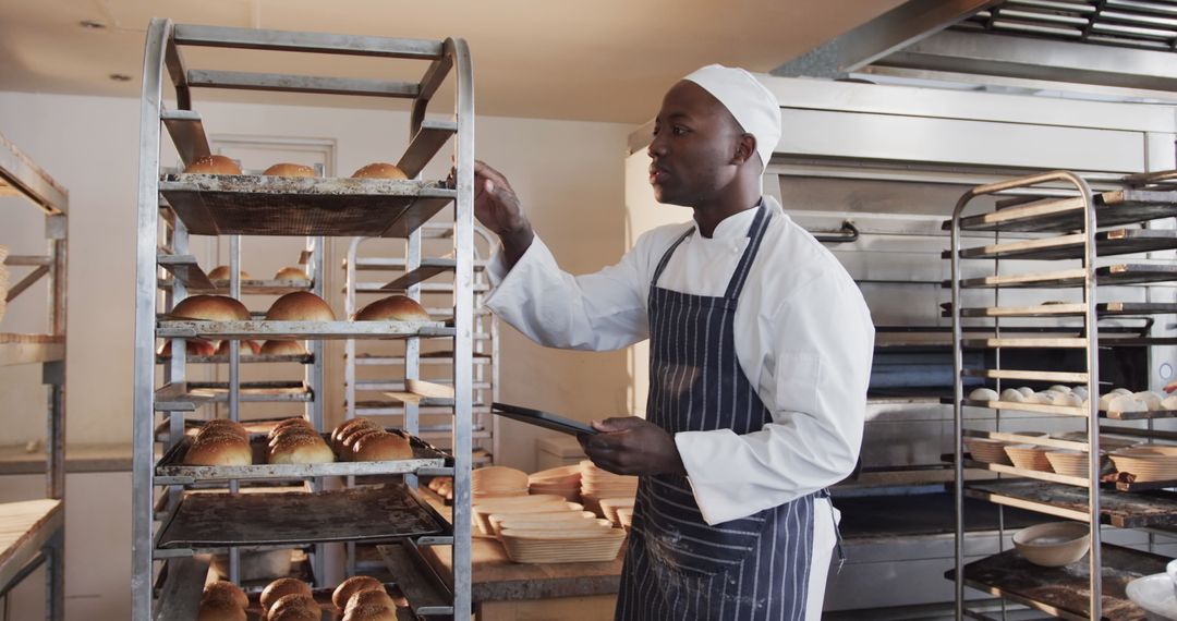 Professional Baker Counts Freshly Baked Bread on Tray Using Tablet