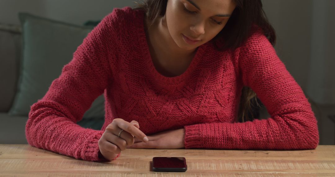 Young Woman Using Touchscreen Smartphone Sitting at Wooden Table at Home - Free Images, Stock Photos and Pictures on Pikwizard.com