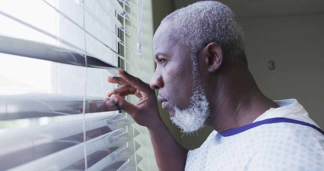 Elderly Man in Hospital Gown Looking Through Window Blinds - Free Images, Stock Photos and Pictures on Pikwizard.com