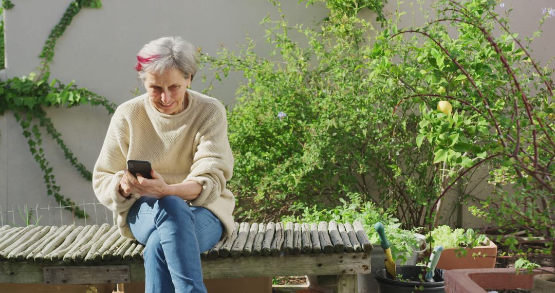 Elderly Woman Sitting in Garden Using Smartphone on Wooden Bench - Free Images, Stock Photos and Pictures on Pikwizard.com