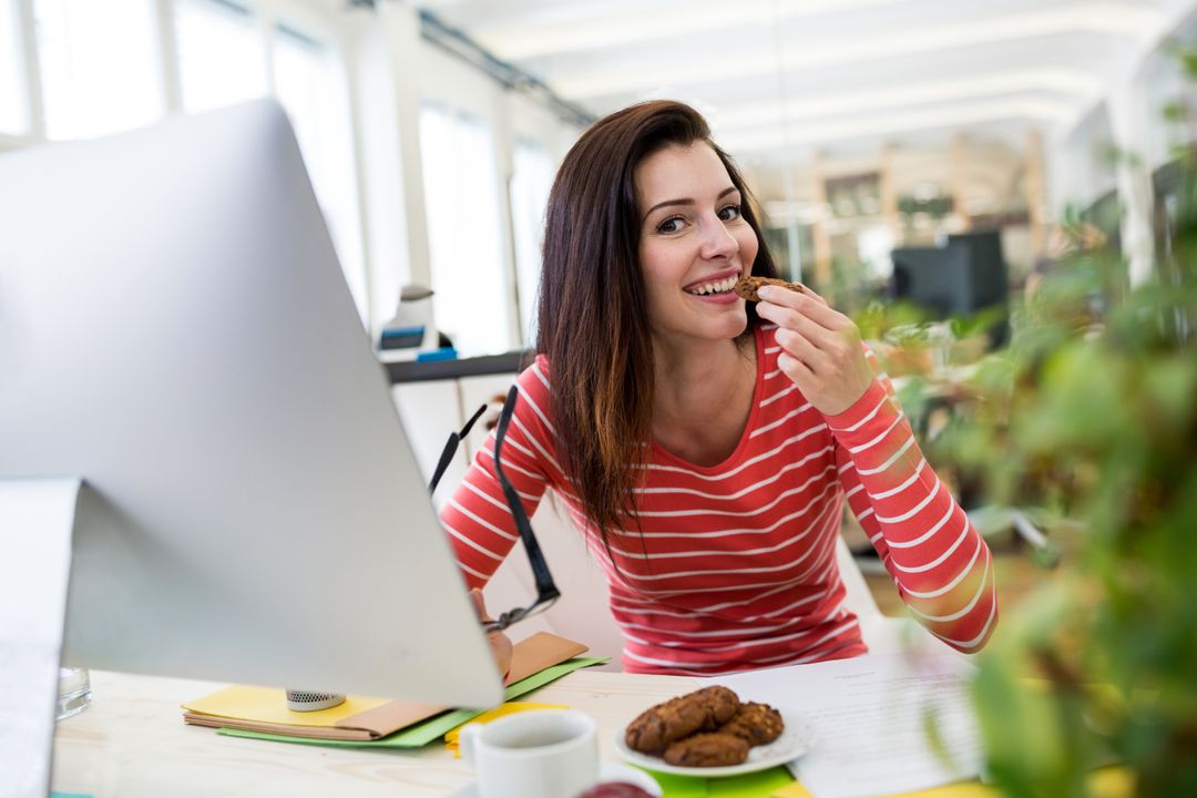 Woman Enjoying Snack While Working at Modern Office Desk