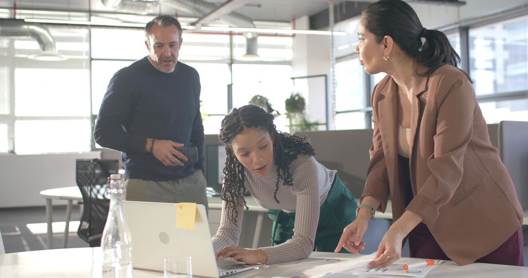 Diverse team collaborating over laptop and documents in modern open-plan office