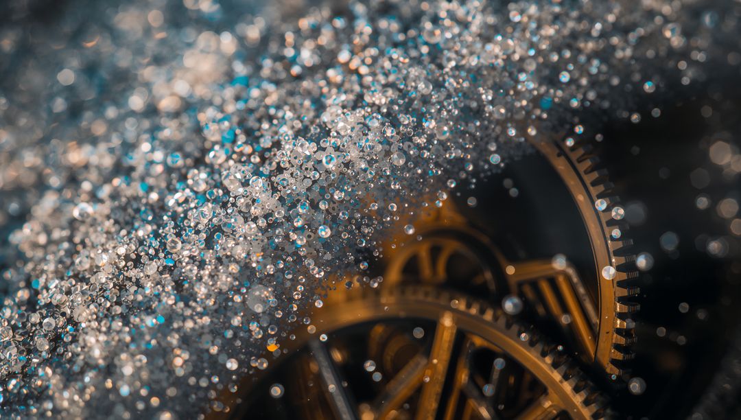 Macro brass clockwork gears reflecting warm studio light with sparkling droplet bokeh