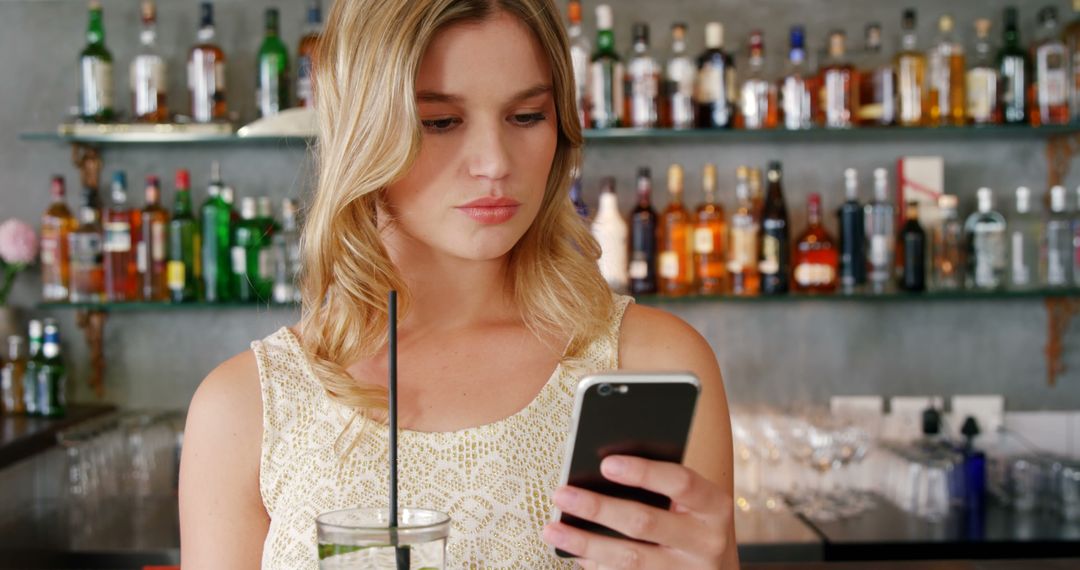 Young Woman Using Smartphone in Bar with Drink and Copy Space