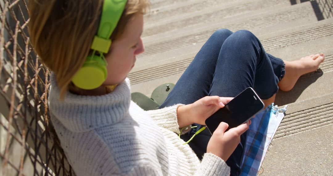 Teen Listening to Music with Headphones While Using Smartphone Outdoors - Free Images, Stock Photos and Pictures on Pikwizard.com