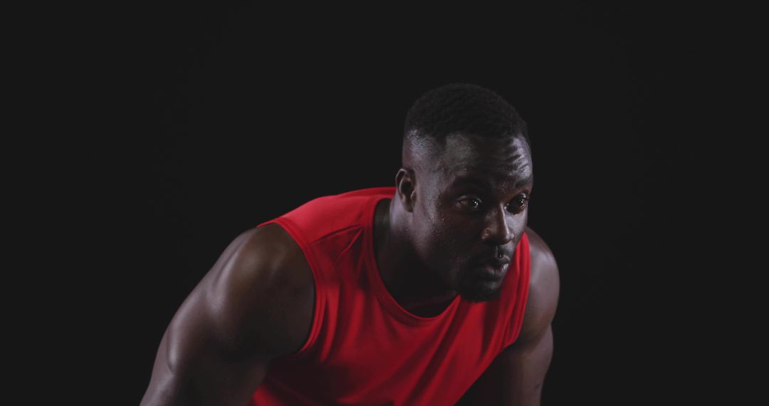 Muscular man leaning forward pushing through fatigue in red sleeveless top intense focus
