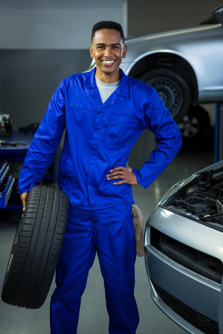 Smiling Mechanic Holding Tire in Auto Repair Garage - Free Images, Stock Photos and Pictures on Pikwizard.com