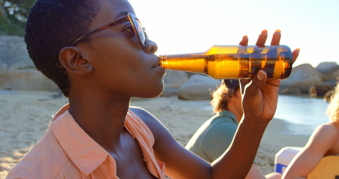 Young woman relaxing on beach with bottle of beer at sunset - Free Images, Stock Photos and Pictures on Pikwizard.com