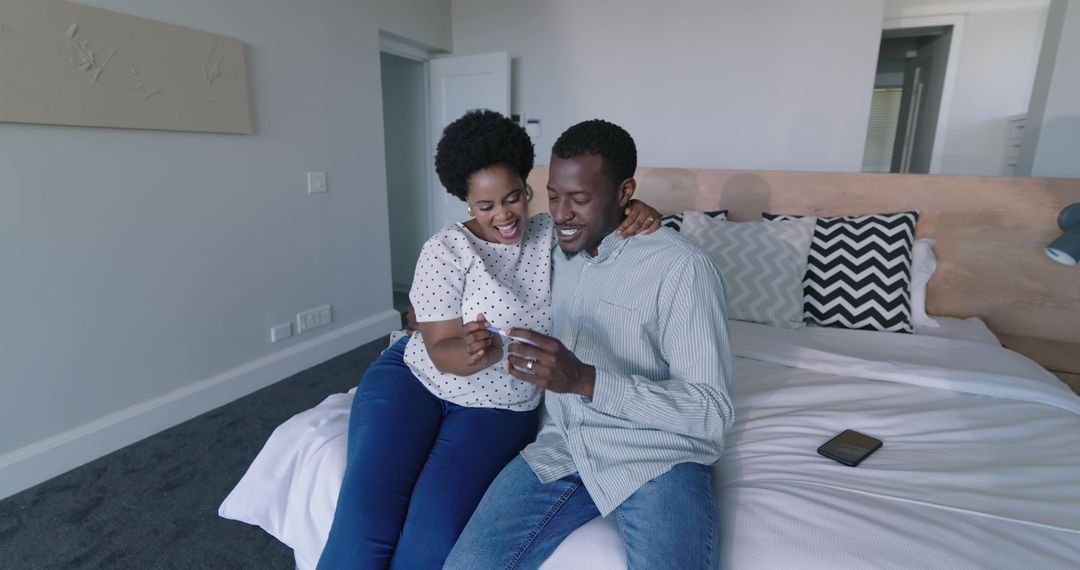 African American Couple Opening Small Gift Box on Bed Celebrating Intimate Moment