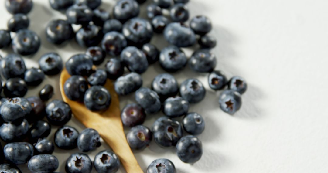 Fresh Blueberries on White Surface with Wooden Spoon - Free Images, Stock Photos and Pictures on Pikwizard.com