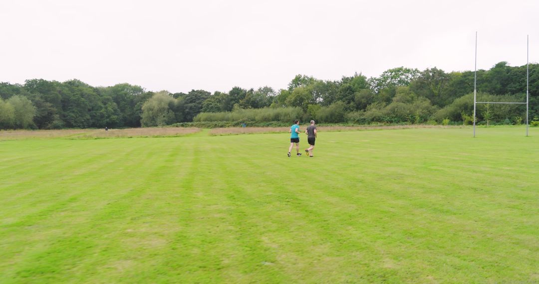 Two Joggers Enjoying Green Field with Lush Trees