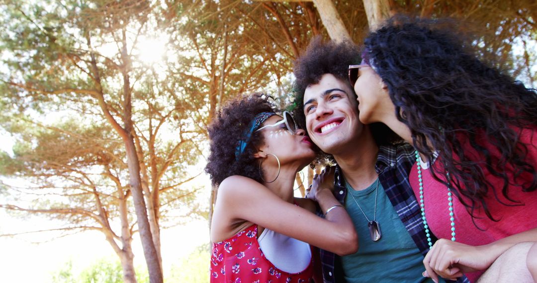 Smiling Young Man Getting Kisses on Cheek from Two Female Friends in Outdoor Park - Free Images, Stock Photos and Pictures on Pikwizard.com