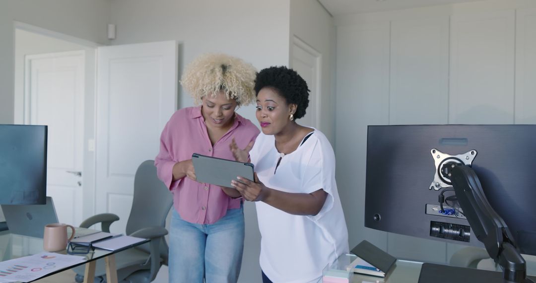 Diverse female coworkers leaning over tablet collaborating on data and charts in office