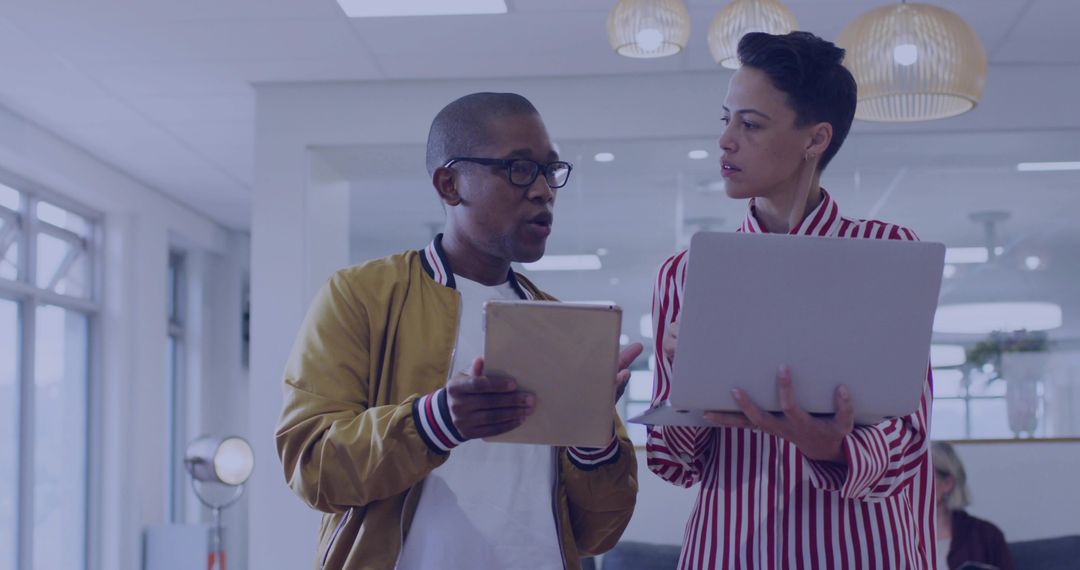 Colleagues Comparing Tablet and Laptop During Collaborative Office Discussion