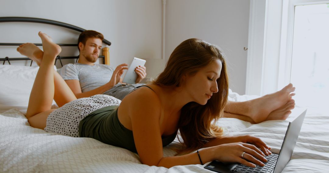 Young Couple Relaxing on Bed with Laptop and Tablet in Cozy Bedroom - Free Images, Stock Photos and Pictures on Pikwizard.com