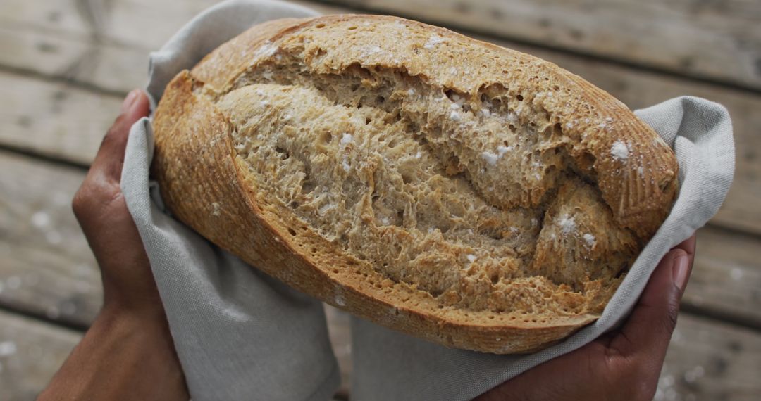 Hands Cradling Freshly Baked Loaf on Rustic Wood Table