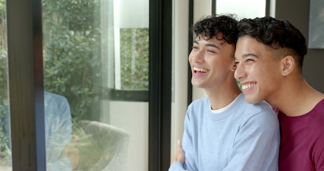 Joyful Asian Couple Standing by Window Overlooking Greenery